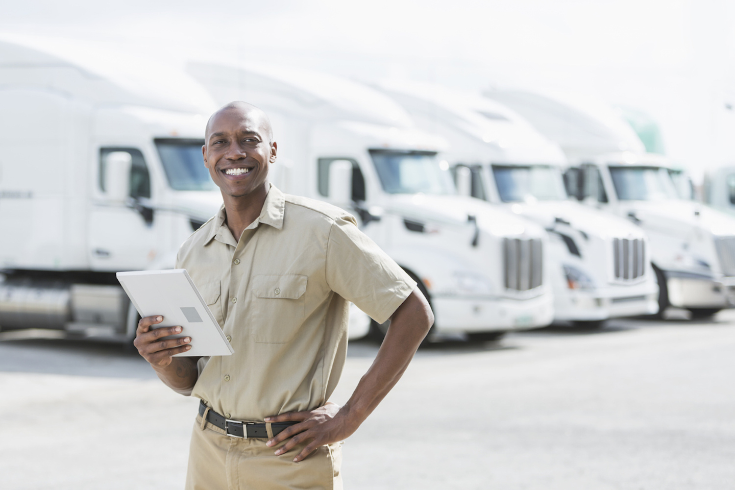 smiling man with computer tablet, standing in front of trucks