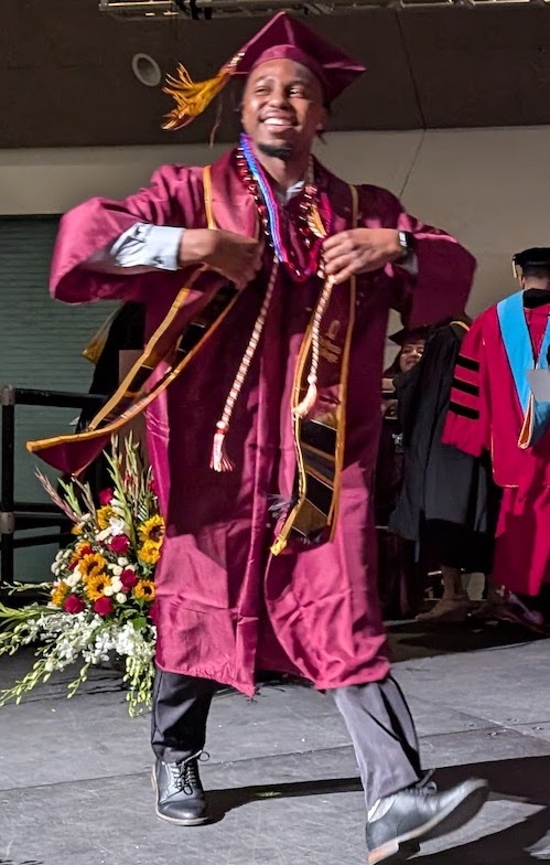 smiling young man in grad cap and gown walking across stage